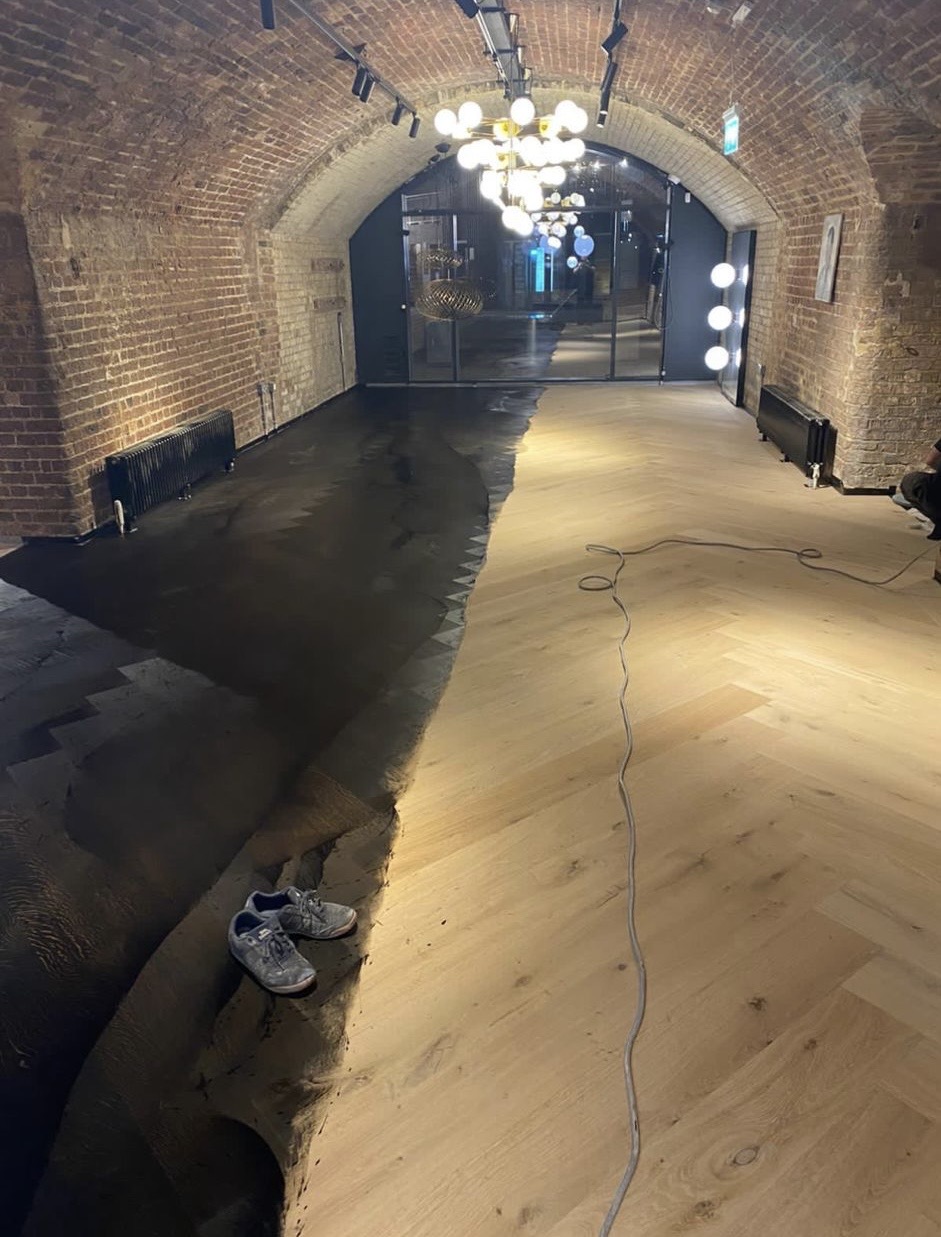 Pale timber flooring adjoining a dark surface in a vaulted brick interior during finishing works.