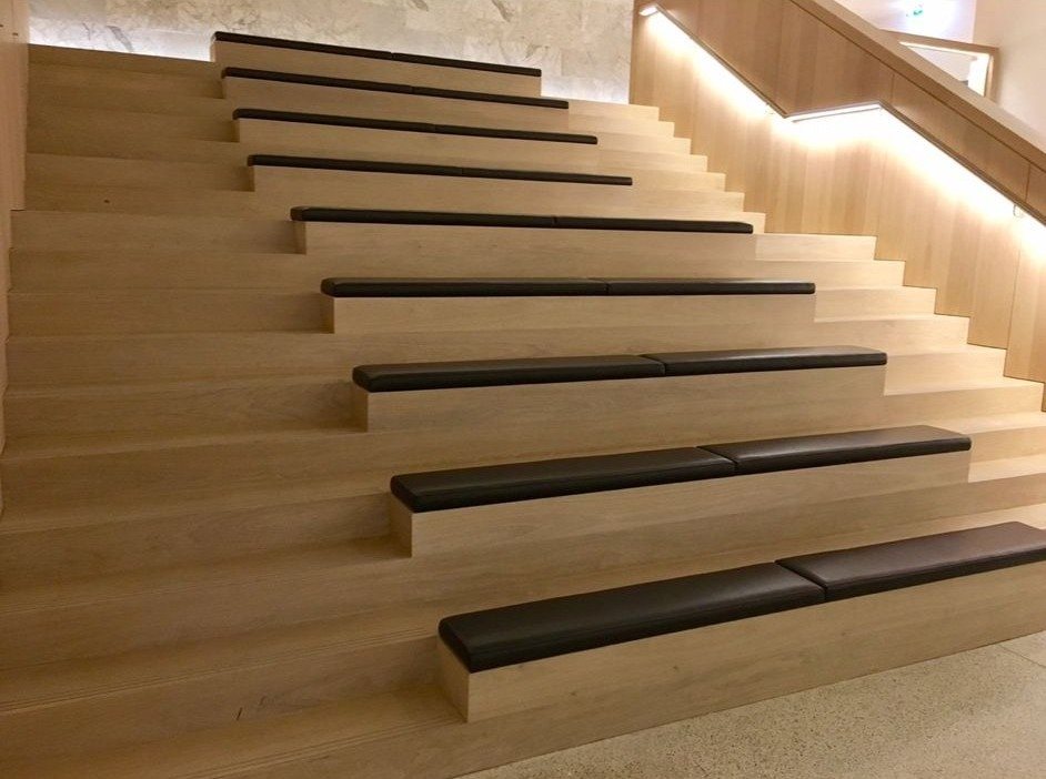 Wide natural timber staircase with dark upholstered seating pads, integrated handrail lighting and contemporary architectural detailing.