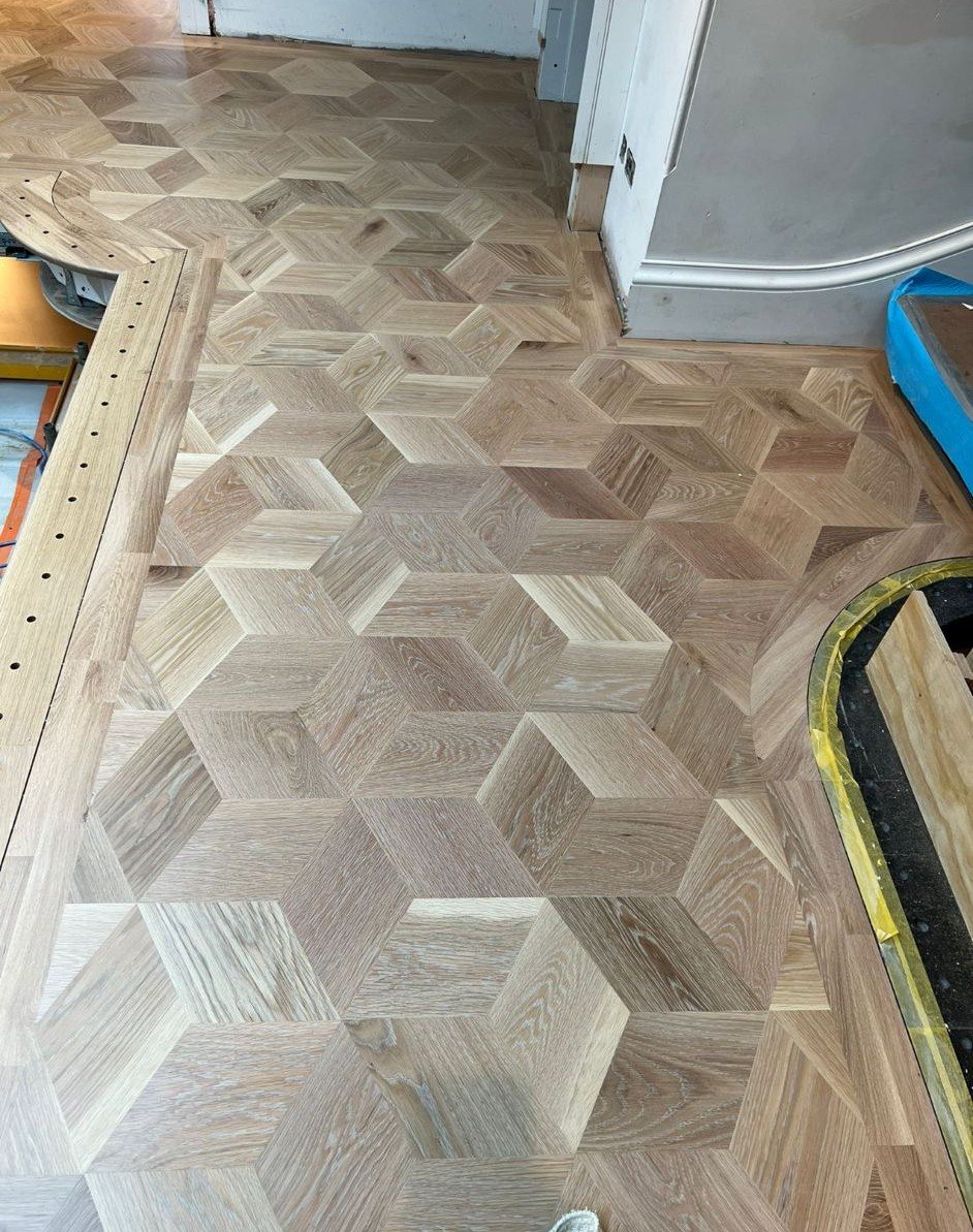 Intricate three-dimensional cube-patterned timber parquet flooring with contrasting grain directions and detailed edging around architectural features.