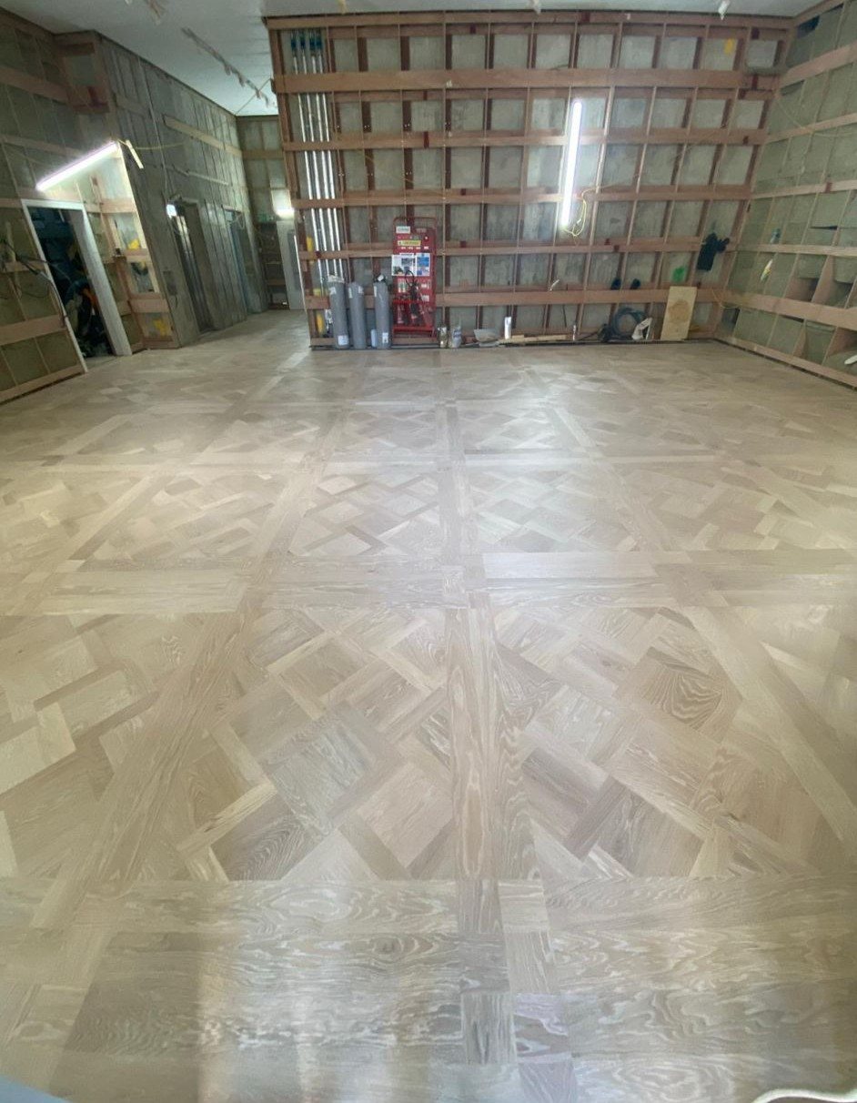 Extensive pale timber parquet flooring featuring large decorative square panels with intricate interwoven geometric patterns inside an interior under refurbishment.