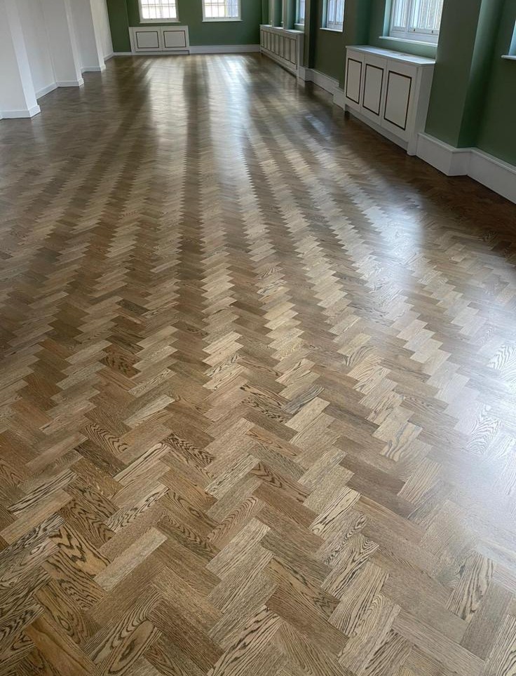 Traditional herringbone timber parquet flooring in a spacious interior with green walls, white panelling and natural daylight.