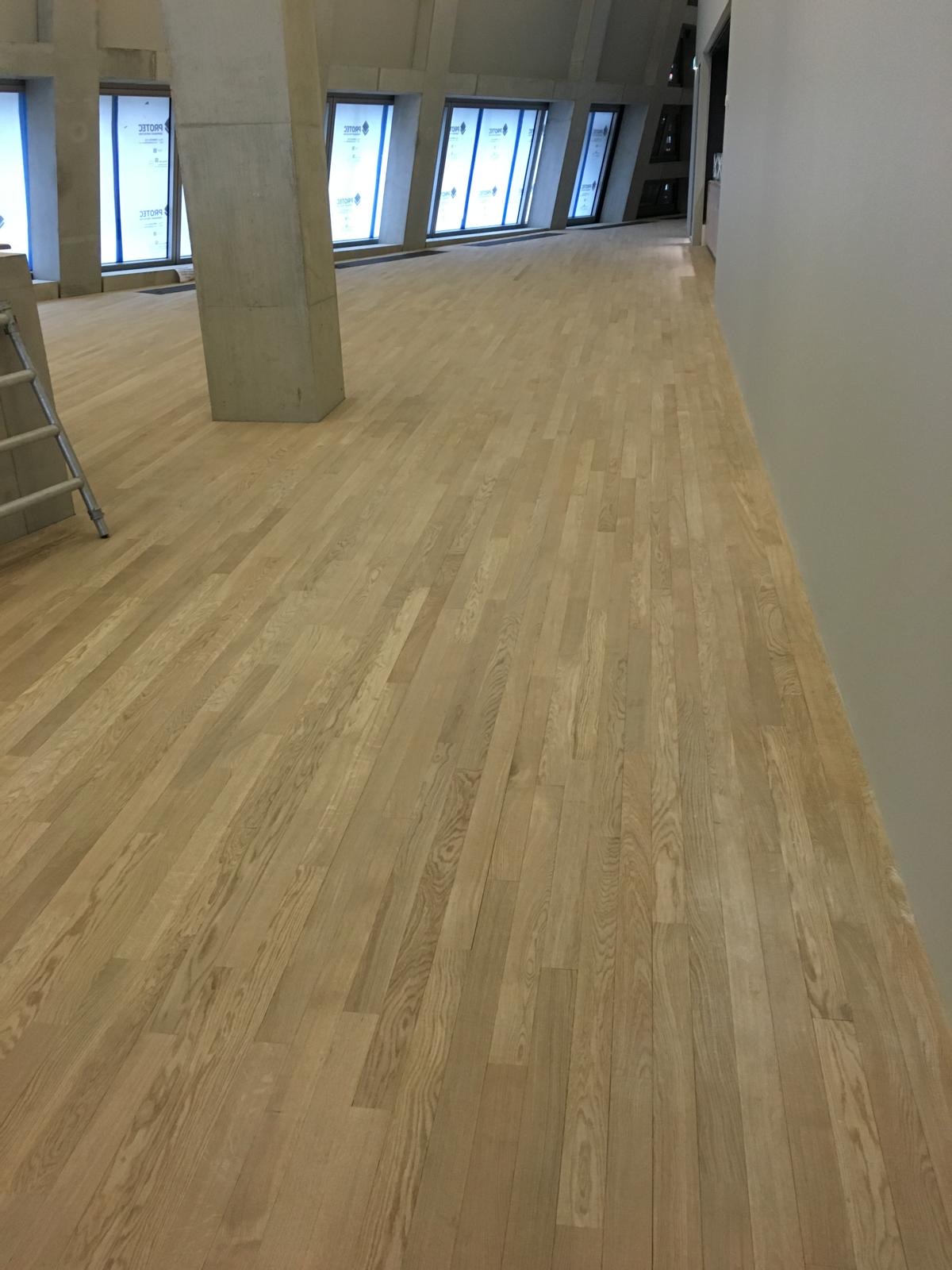 Extensive light natural timber flooring in a contemporary architectural space with angled concrete columns and tall windows.