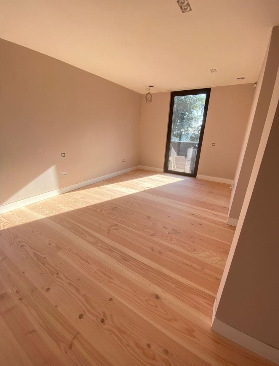 Light natural wide-plank timber flooring in a contemporary residential room with soft neutral walls and a full-height glazed door.