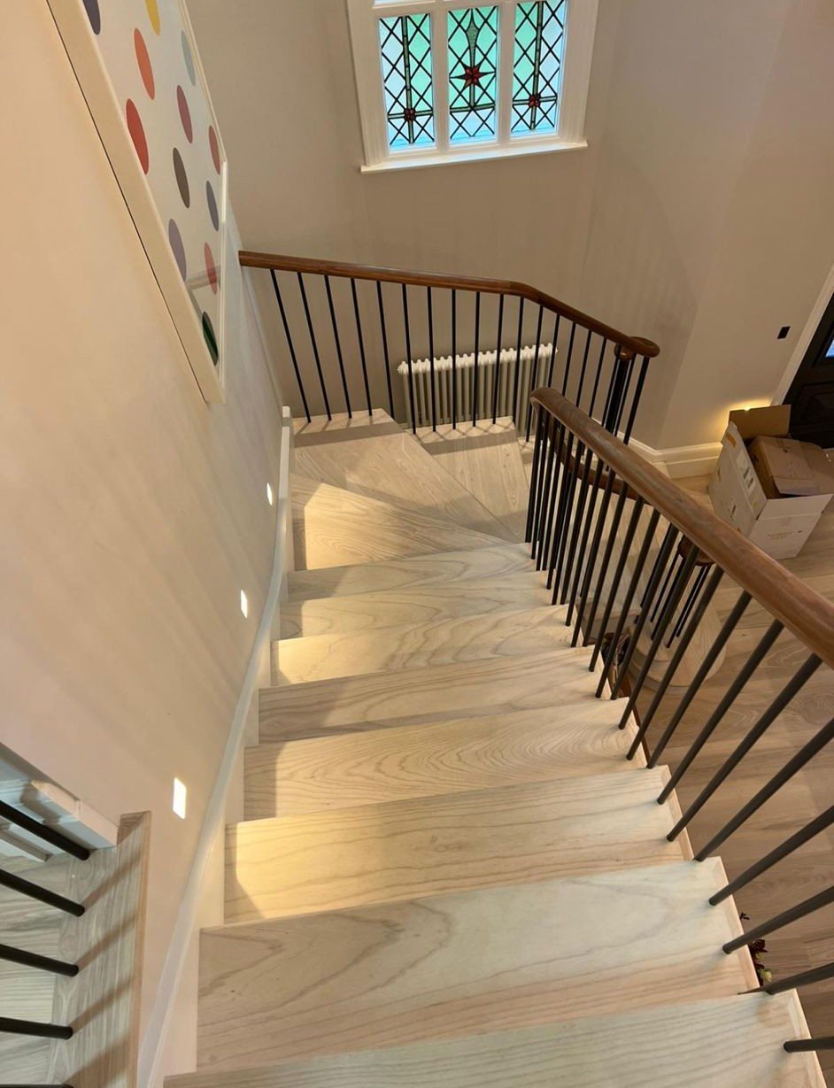 Pale natural timber staircase with integrated step lighting, black metal balustrade, timber handrail and decorative stained-glass window.