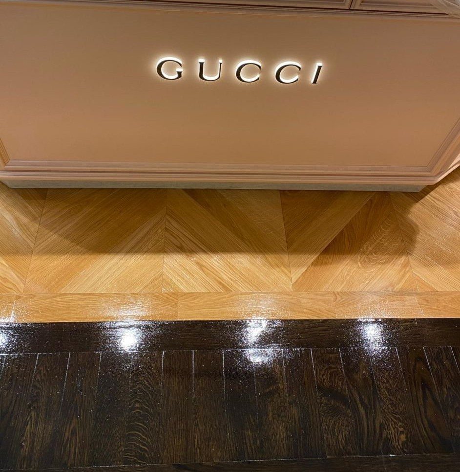 Chevron-patterned timber flooring transitioning from a natural oak-toned finish to dark-stained timber in a luxury retail interior.