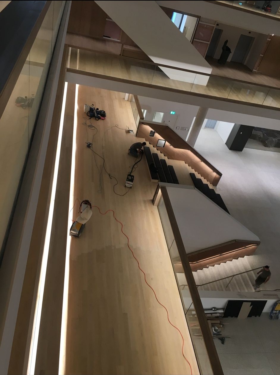 Overhead view of floor sanding equipment and a worker on a timber floor in a multi-level interior.