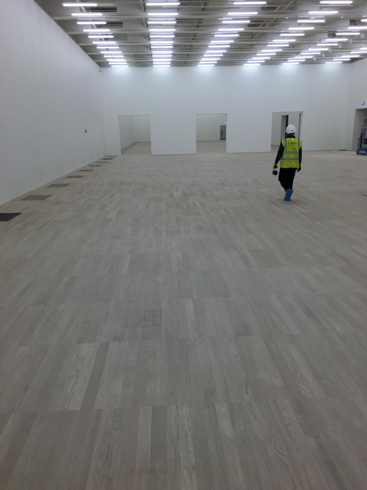 Pale timber plank flooring extending across a large white-walled interior during construction works.