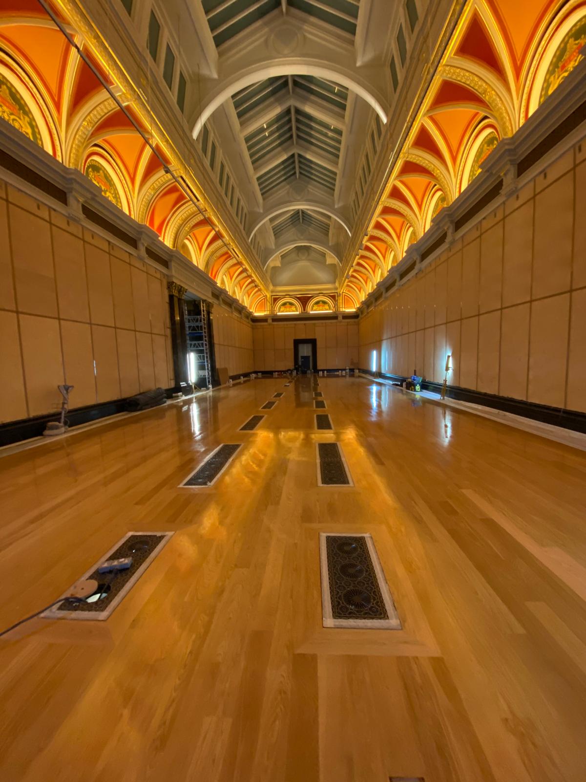 Polished timber flooring in a long ornate hall with a vaulted ceiling and decorative floor grilles.