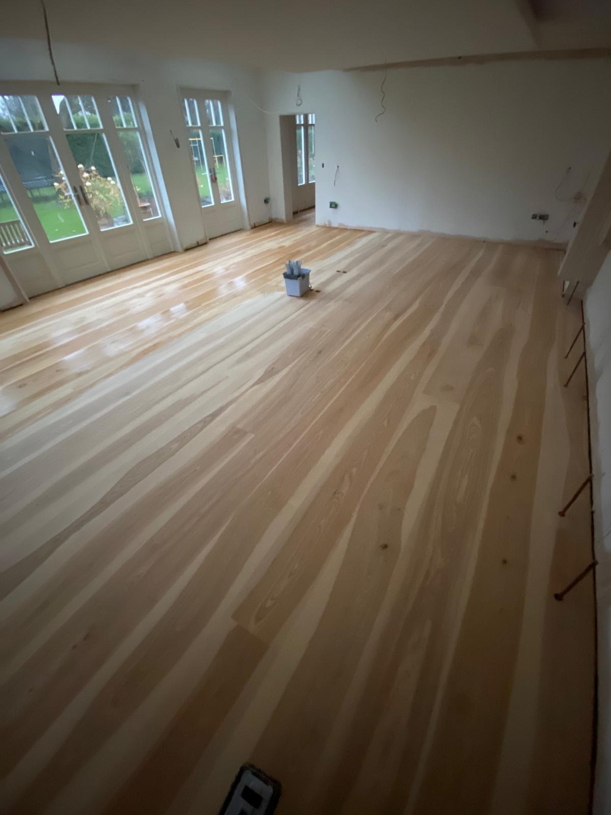 Light natural timber plank flooring extending across a spacious residential interior with glazed garden doors.