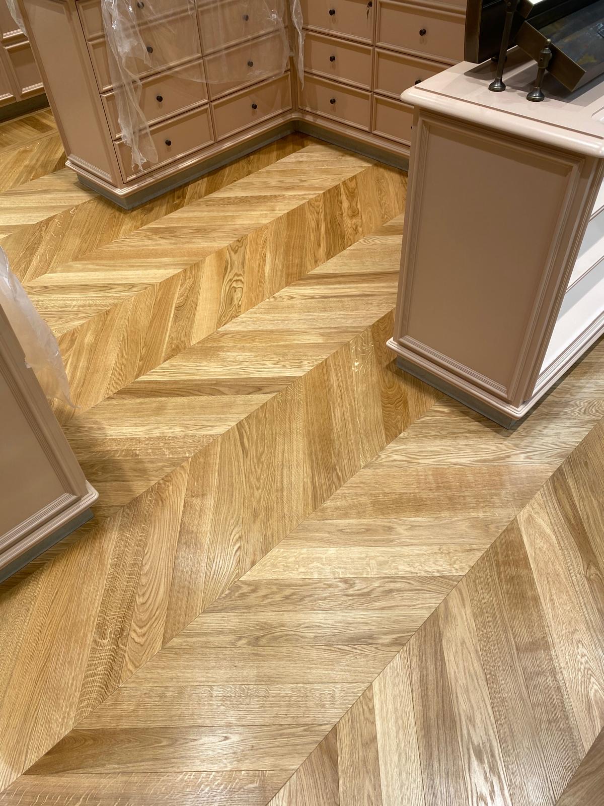 Wide chevron-patterned timber floor with contrasting grain tones beside pale fitted cabinetry.