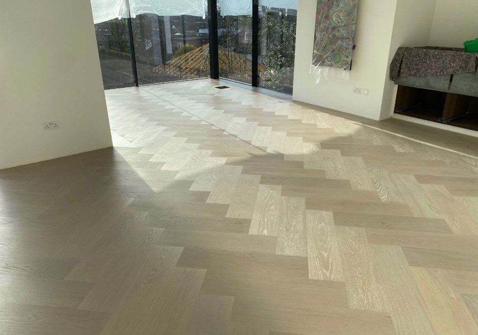 Pale herringbone timber parquet flooring across a bright contemporary interior with floor-to-ceiling glazing and natural daylight.