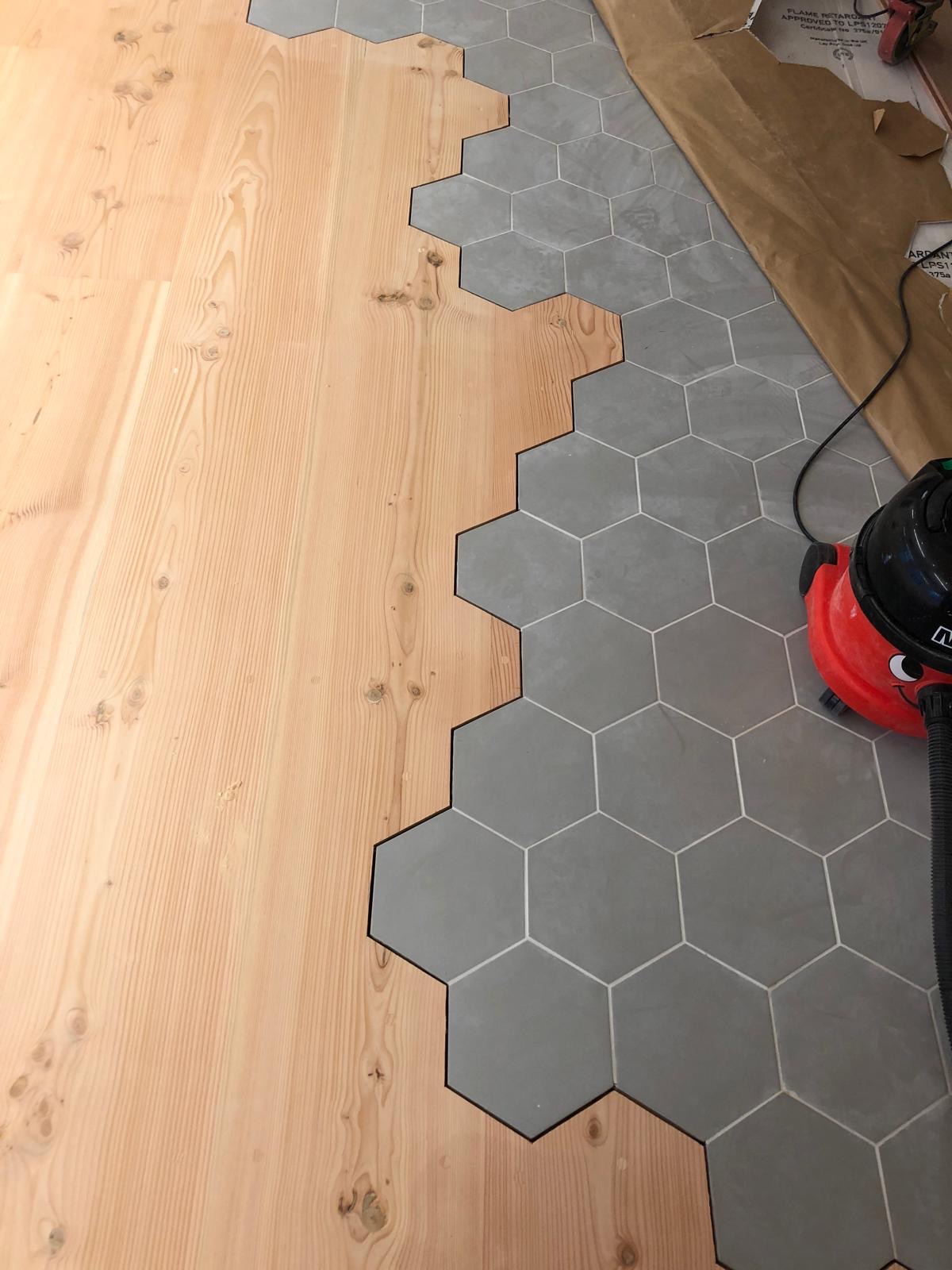 Detailed transition between light natural timber floorboards and grey hexagonal floor tiles with a precisely shaped interlocking edge.